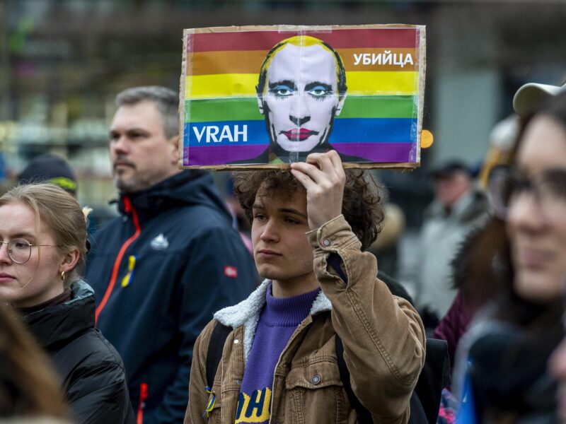 Photo of a man holding a drawing of Putin wearing make up against a rainbow background, as part of an anti Russian invasion protest in ​Teplice, Czech Republic, on March 4