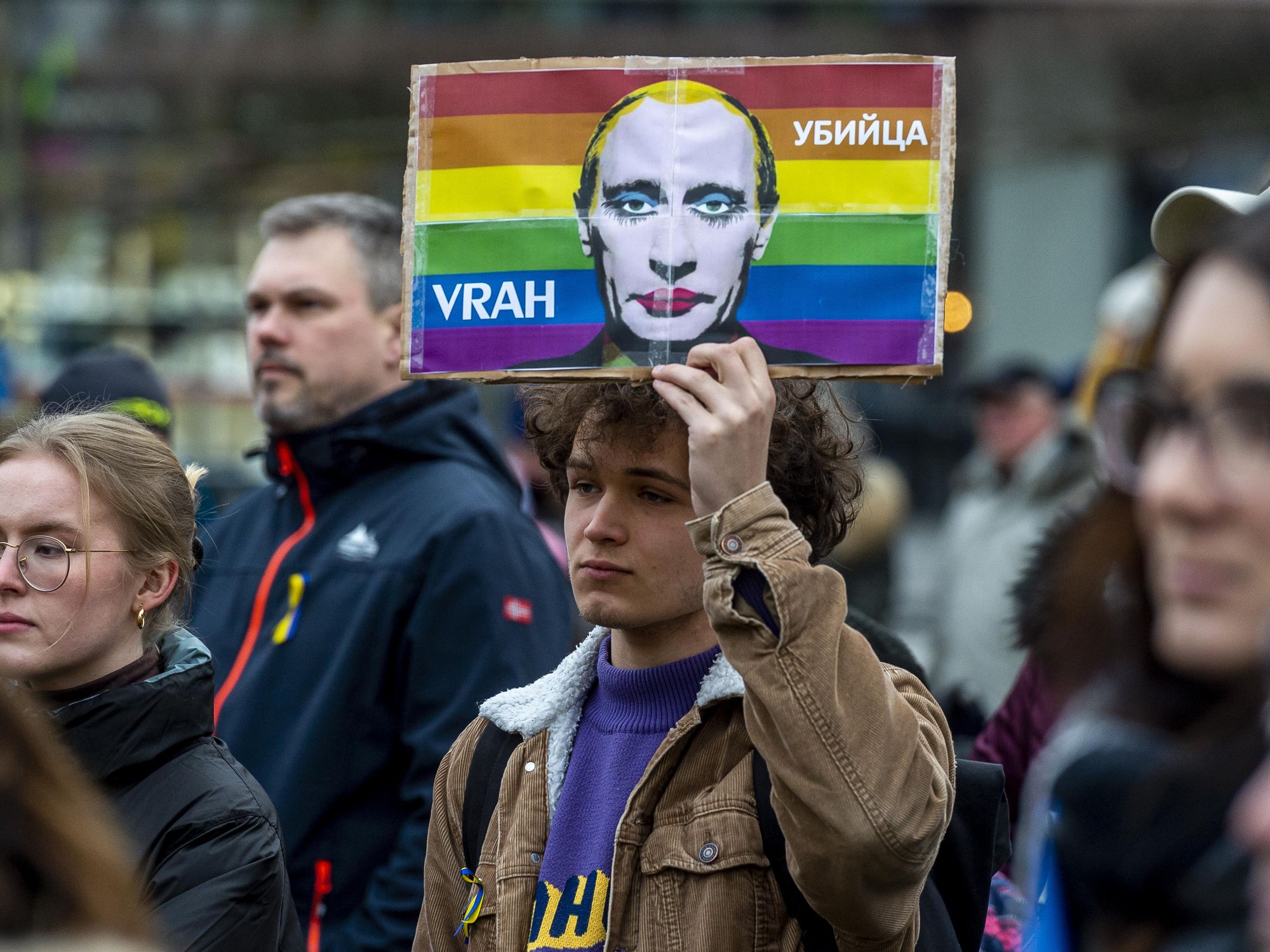 Photo of a man holding a drawing of Putin wearing make up against a rainbow background, as part of an anti Russian invasion protest in ​Teplice, Czech Republic, on March 4