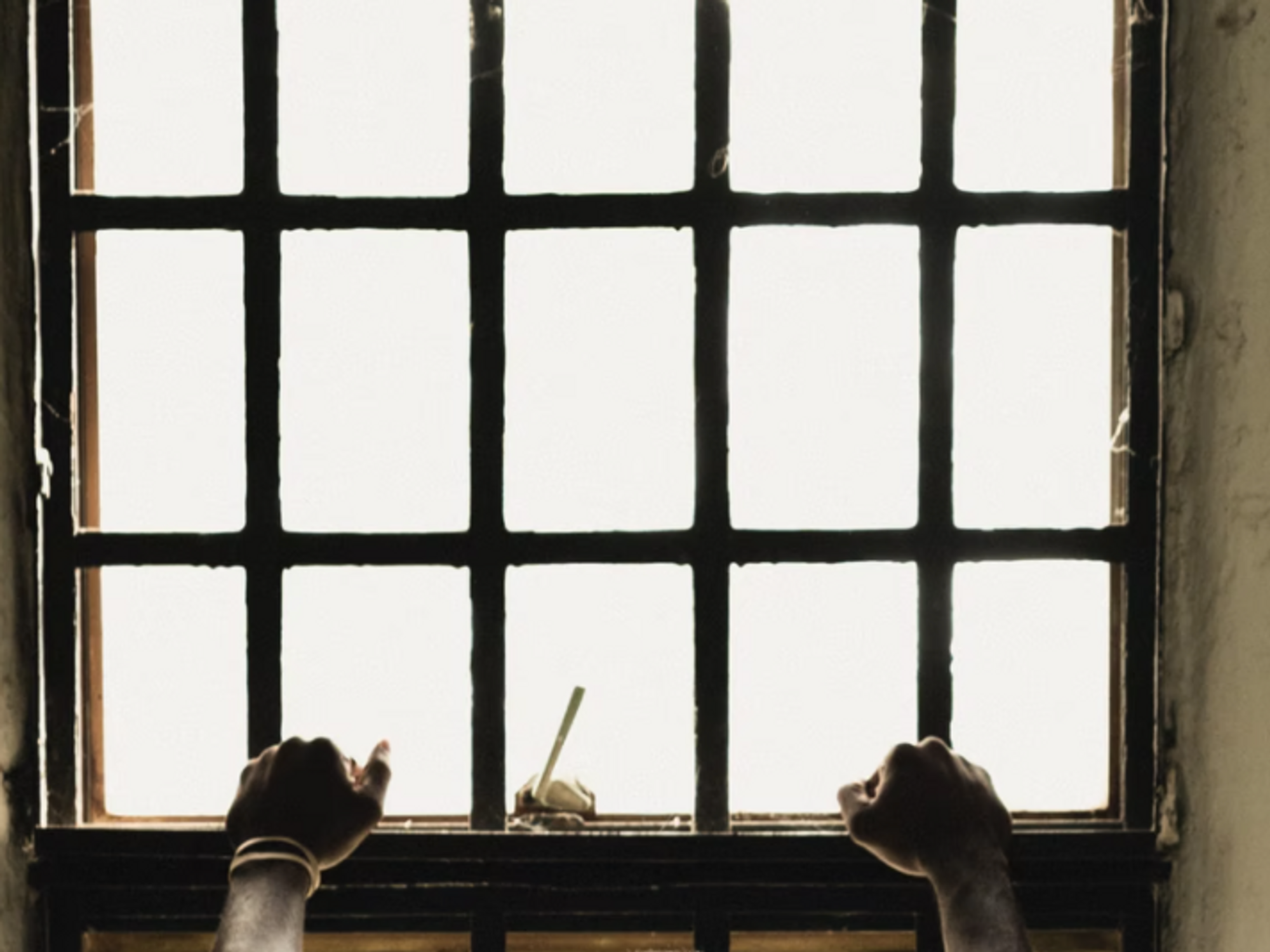 Photo of a man holding prison bars in his cell