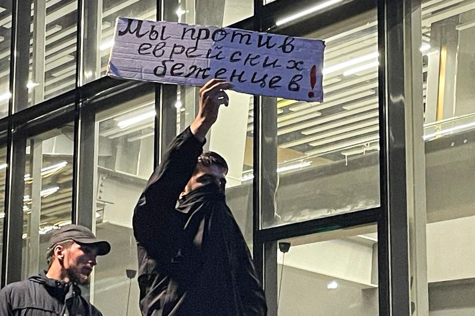 Photo of a man holding up a sign "We are against Jewish refugees"