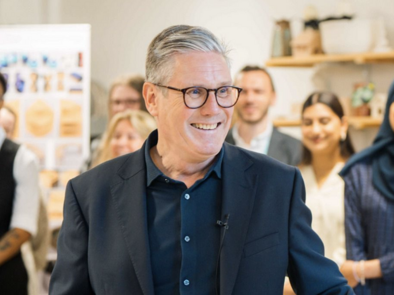 Photo of a man in a suit smiling with his back to a group of 7 people