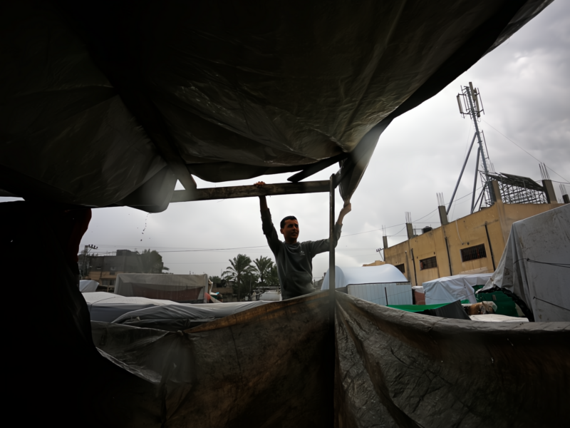 Photo of a man installing a tarp over a tent structure in Gaza