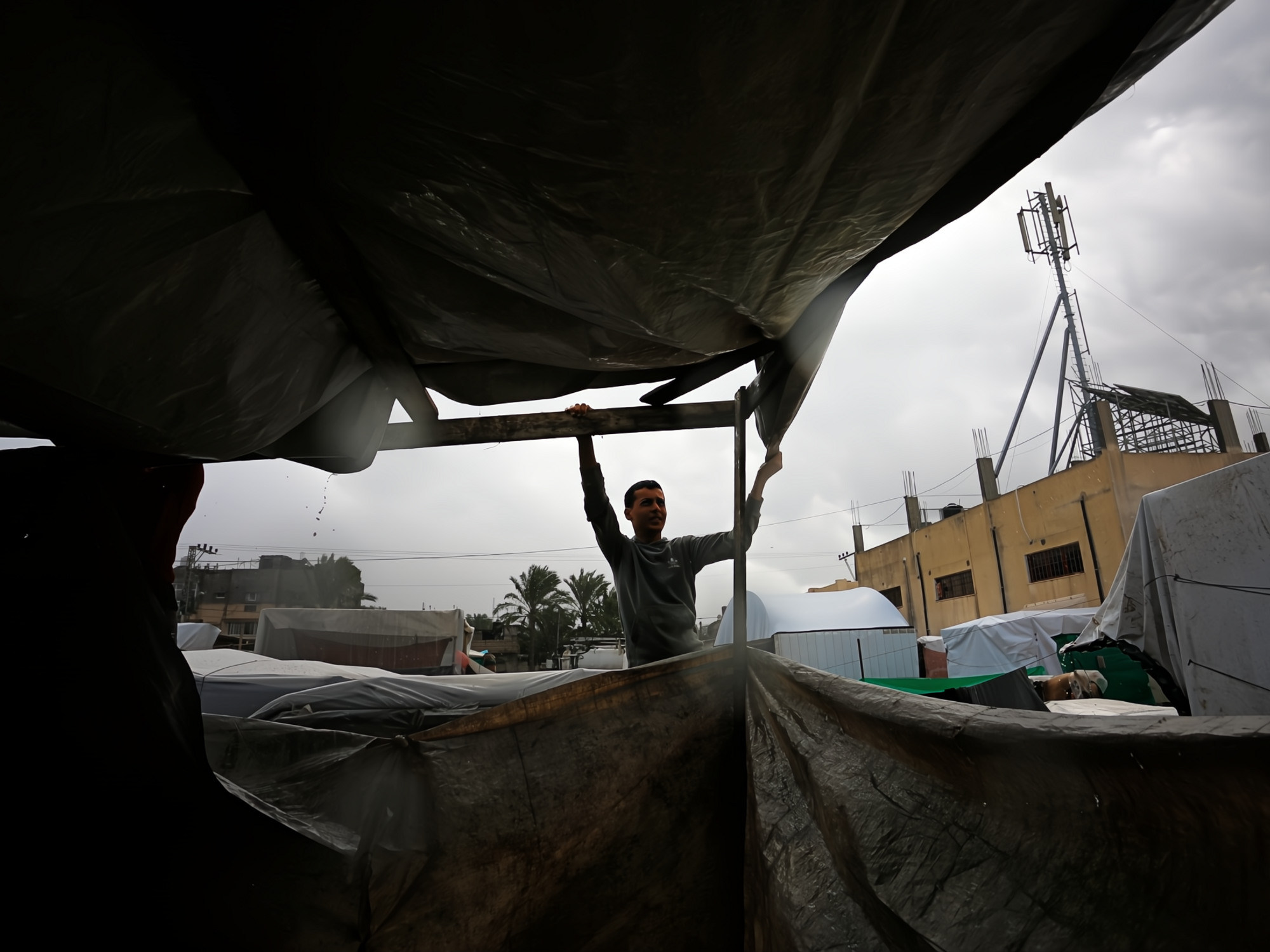 Photo of a man installing a tarp over a tent structure in Gaza