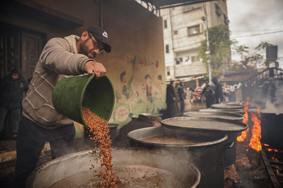 Photo of a man pouring food in big pots during a meal distribution in Rafah, Gaza, on Jan. 27