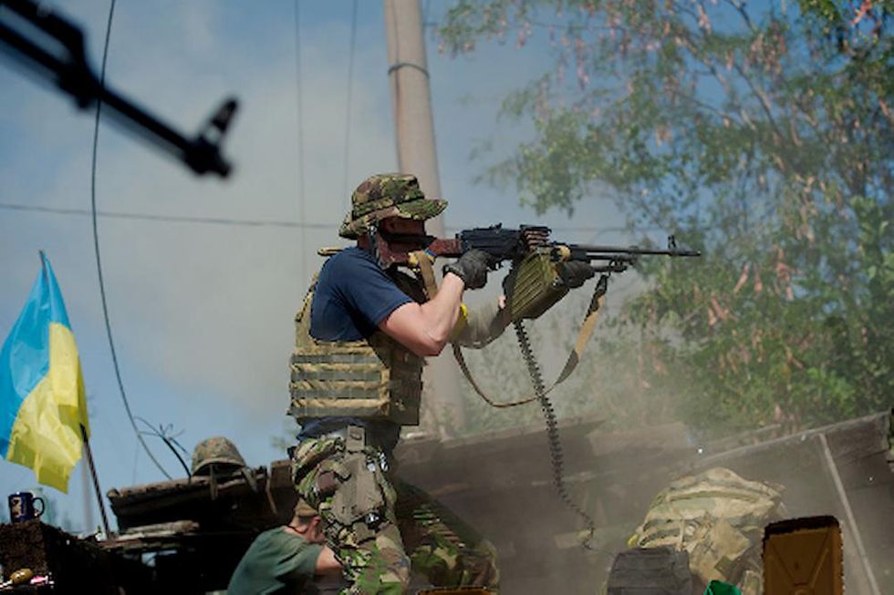 Photo of a man shooting an automatic rifle, with a Ukrainian flag on the left of the image