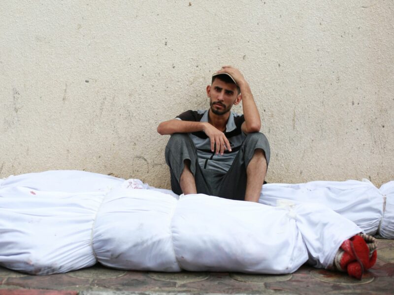 Photo of a man sitting down next to bodies wrapped in white bags
