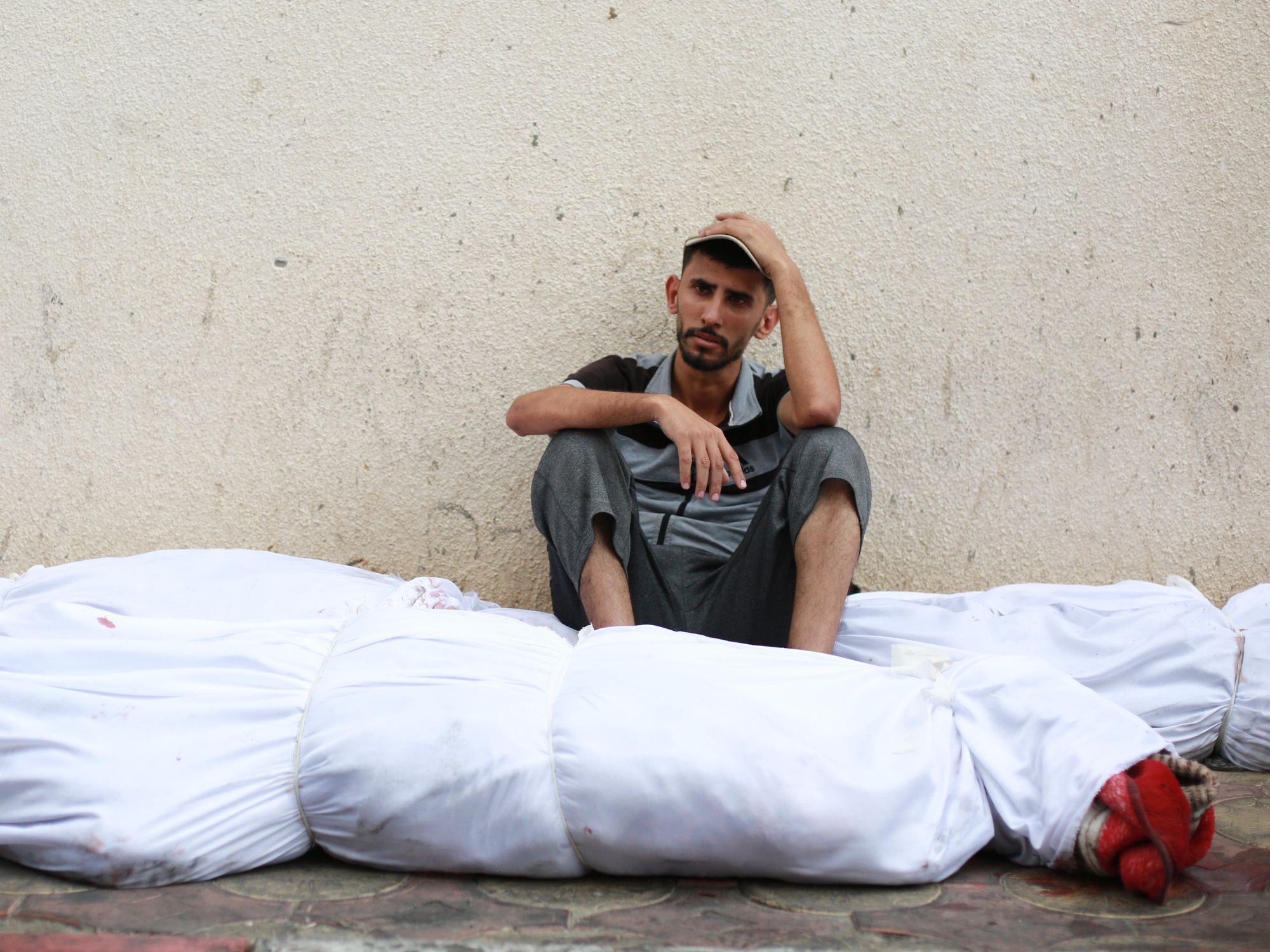 Photo of a man sitting down next to bodies wrapped in white bags