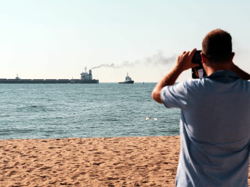 Photo of a man taking a photo from a beach of ships leaving the port of Chornomorsk