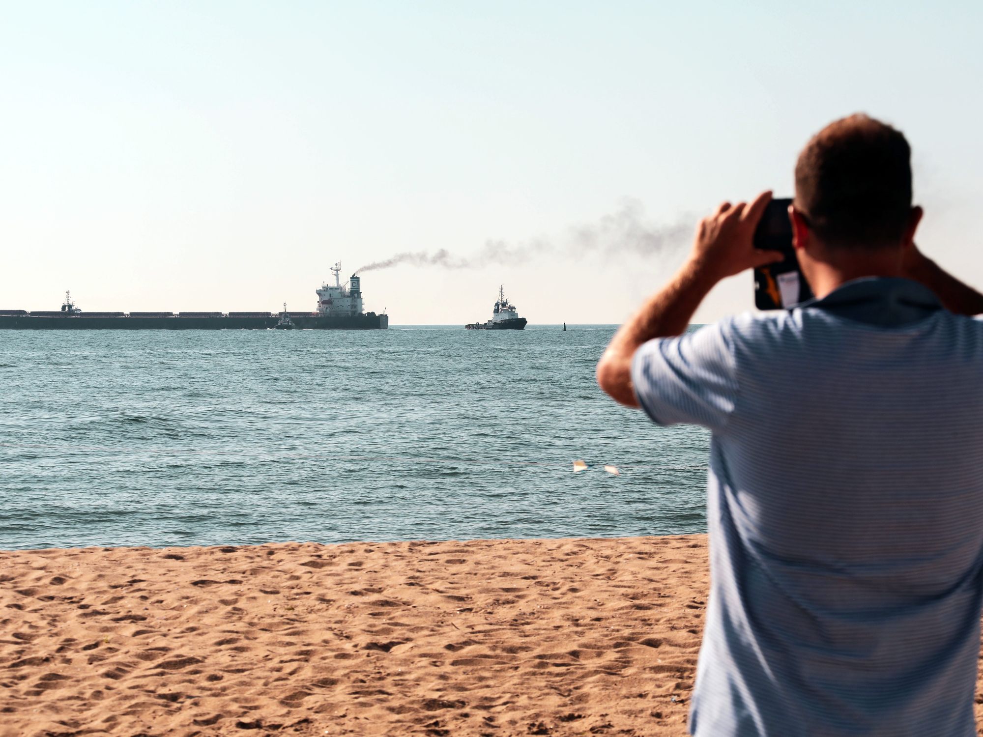 Photo of a man taking a photo from a beach of ships leaving the port of Chornomorsk