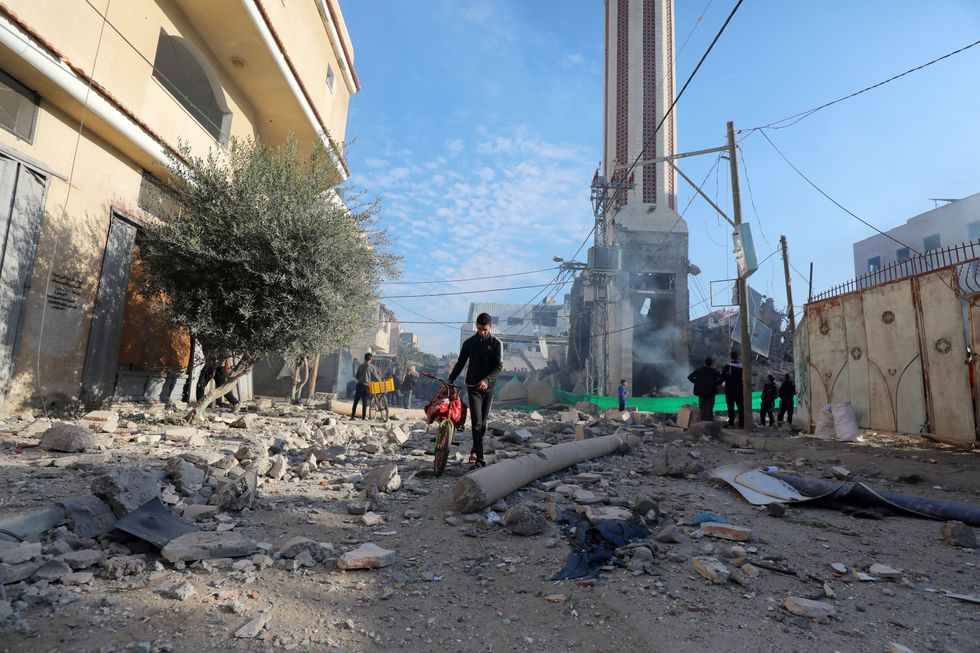 Photo of a man walking beside his bicycle in a destroyed part of Dair El-Balah, Gaza.