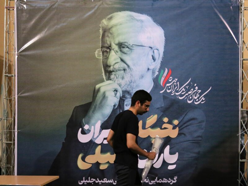 Photo of a man walking past a Saeed Jalili poster