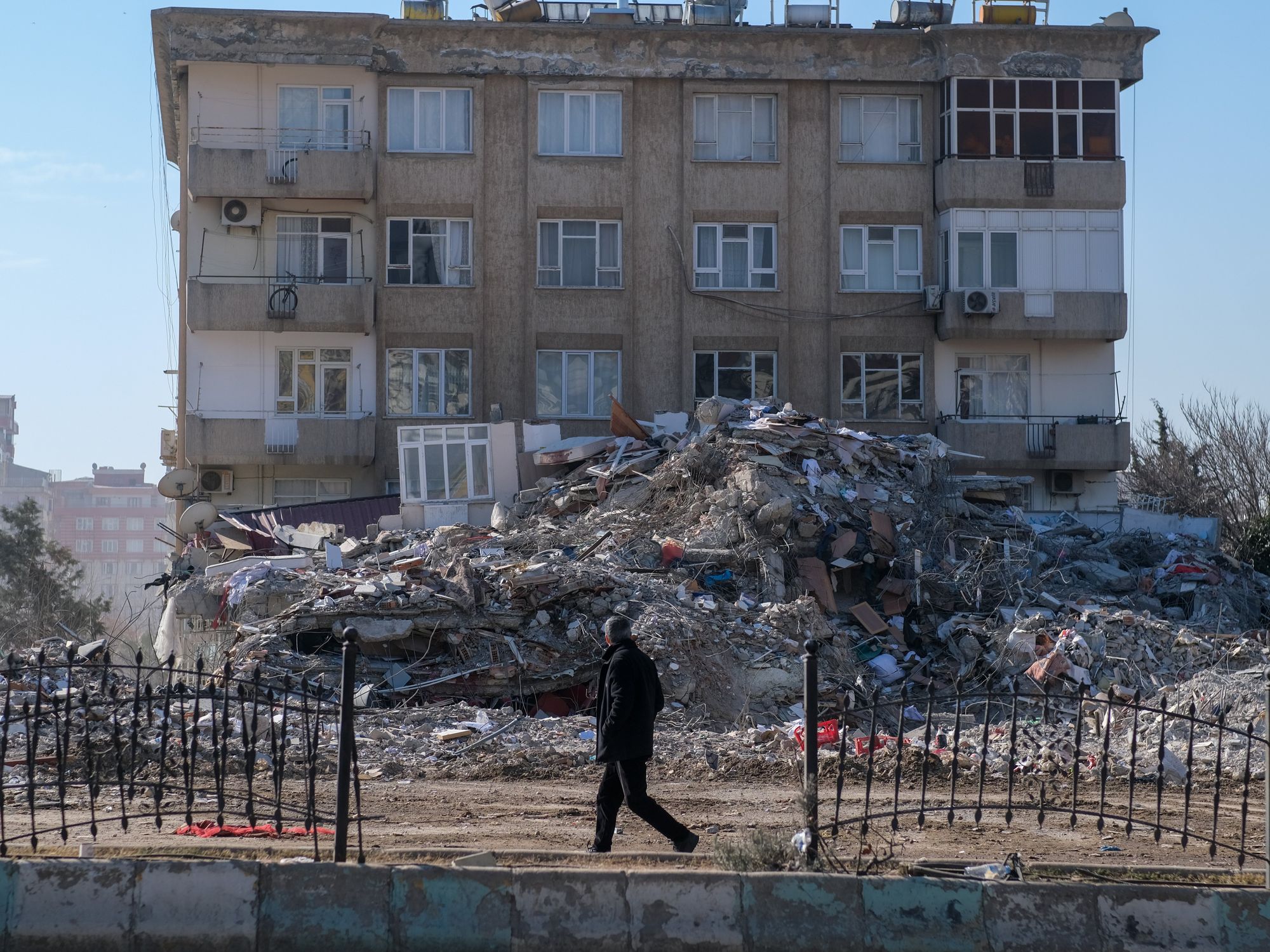 Photo of a man walking past destroyed buildings in ​Kahramanmaras, Turkey, on Feb. 15