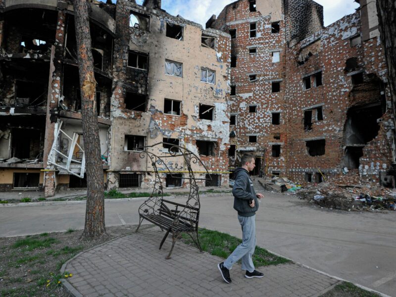 Photo of a man walking past destroyed houses in Irpin