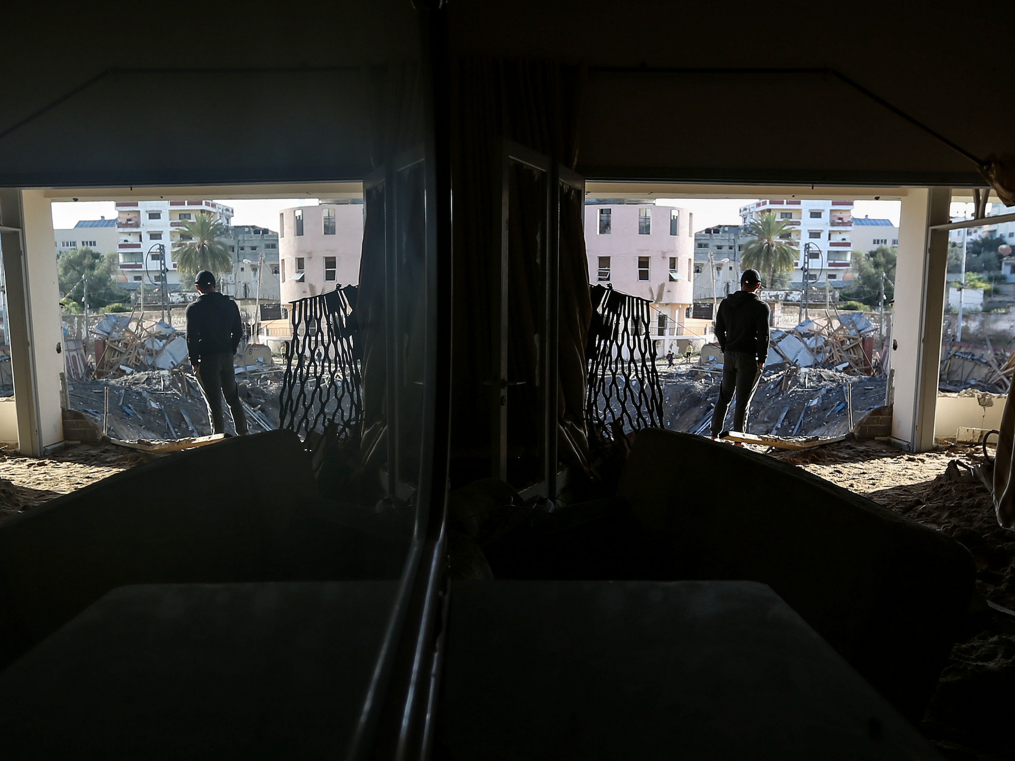 Photo of a man watching over debris left by an airstrike on Gaza City. The scene is reflected in a mirror on the wall of an apartment.
