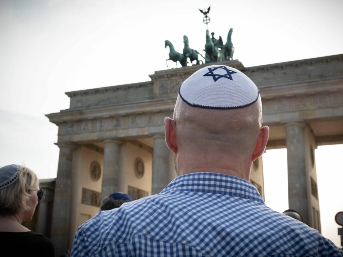 Photo of a man wearing a kippah with a Star of David, standing in front of Berlin Brandenburg Gate during a rally against anti-semitism Berlin