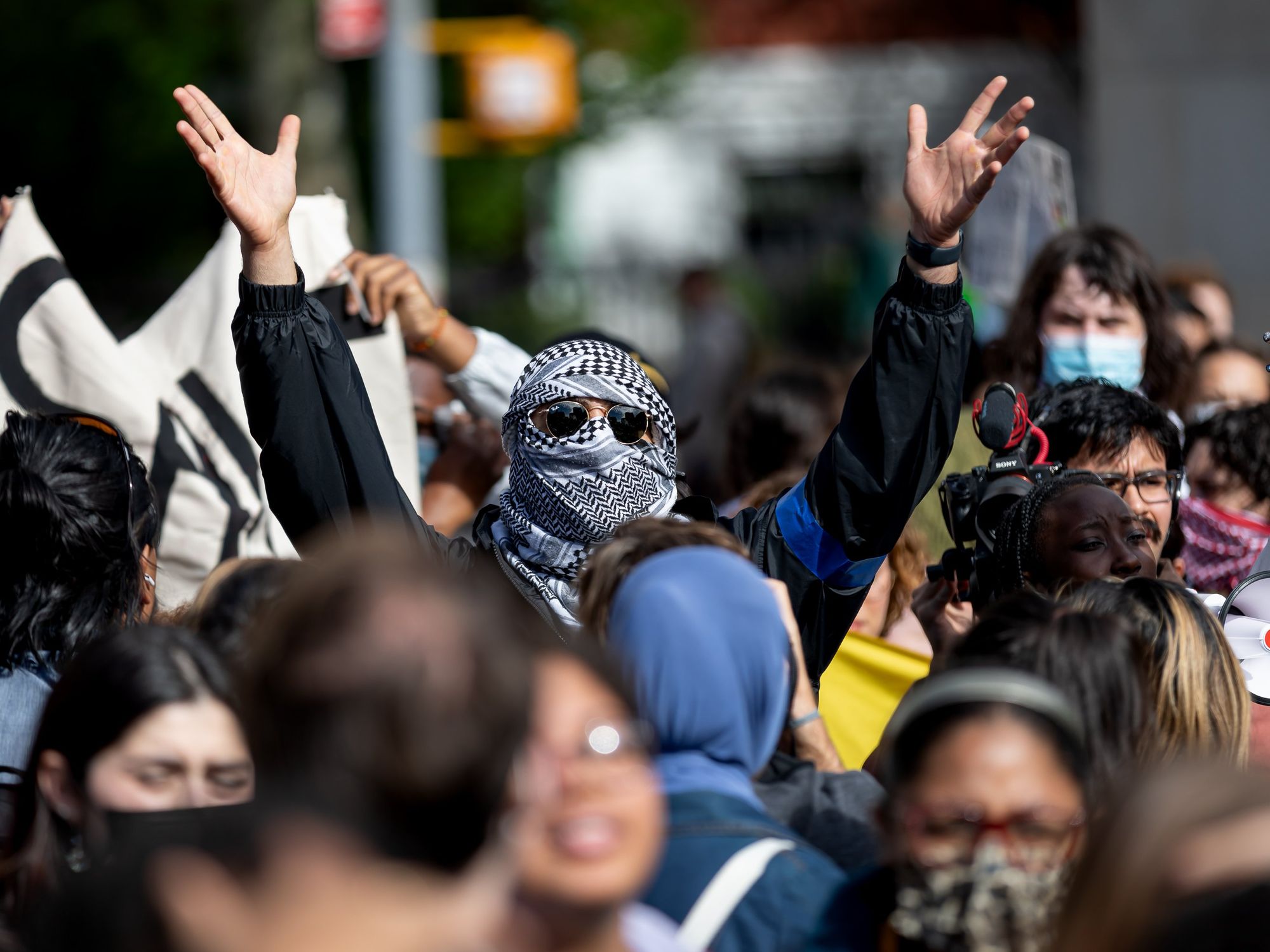 Photo of a man wearing a Palestinian headgarb, raising his hands as part of an Oct. 25 protest calling for a ceasefire in Gaza, in New York