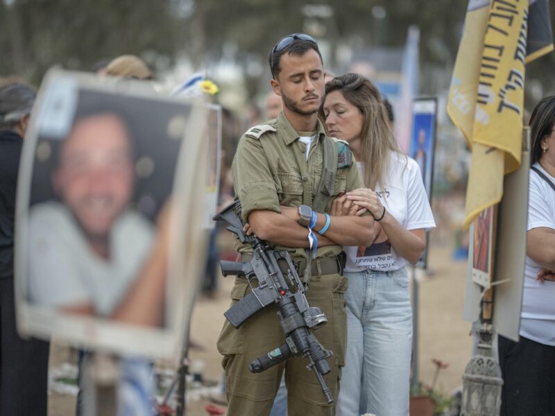 Photo of a man wearing a rifle and a woman mourning as they mark one yearsince Hamas Oct. 7 attack on Israel at the site of the Nova Festival.
