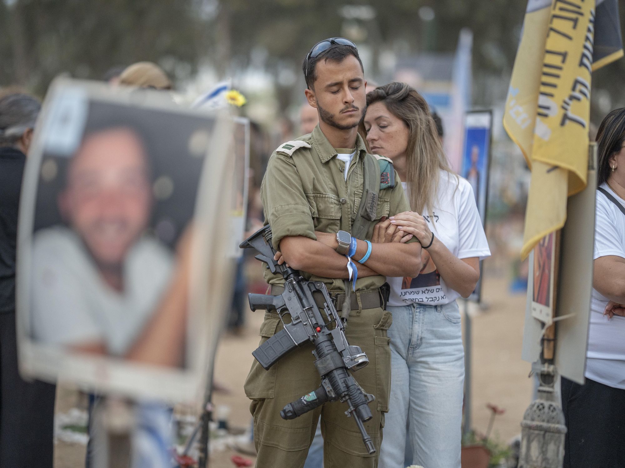 Photo of a man wearing a rifle and a woman mourning as they mark one yearsince Hamas Oct. 7 attack on Israel at the site of the Nova Festival.