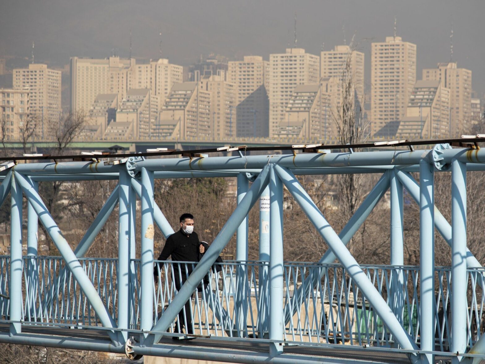 photo of a man with a mask crossing a blue foot bridge
