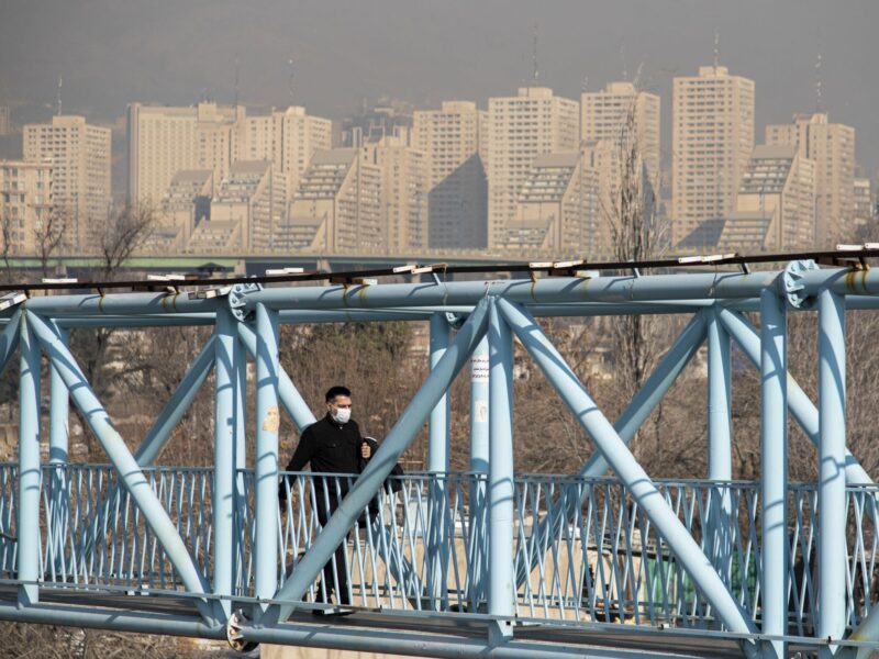photo of a man with a mask crossing a blue foot bridge