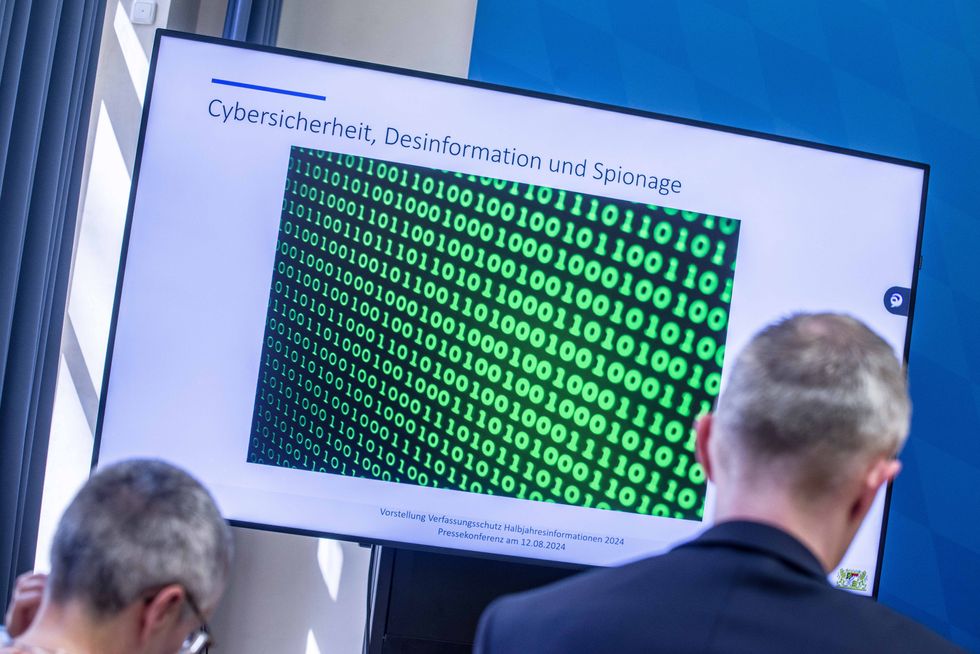 Photo of a meeting at the German Secret Services showig a slide projected on a screen, depicting lines of code to illustrate cybersecurity, disinformation and espionage