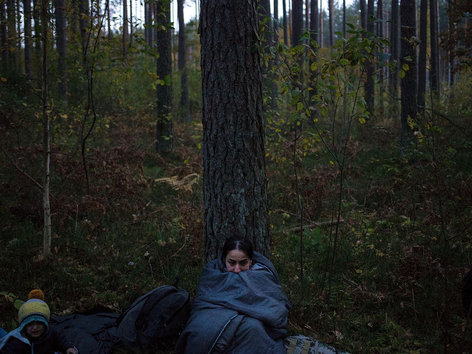 Photo of a migrant woman in a sleeping bag, sitting in a forest in Michalowo, Belarus, next to the border with Poland.​