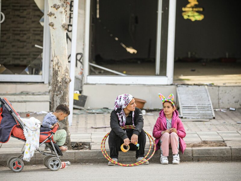 Photo of a mother and two children sitting on the sidewalk.