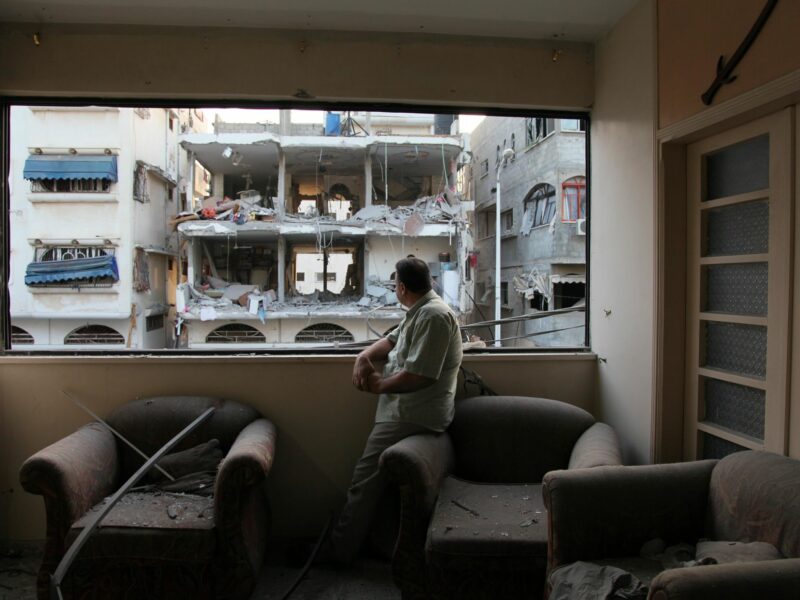 Photo of a Palestinian man in Gaza looking out the window of a destroyed building.