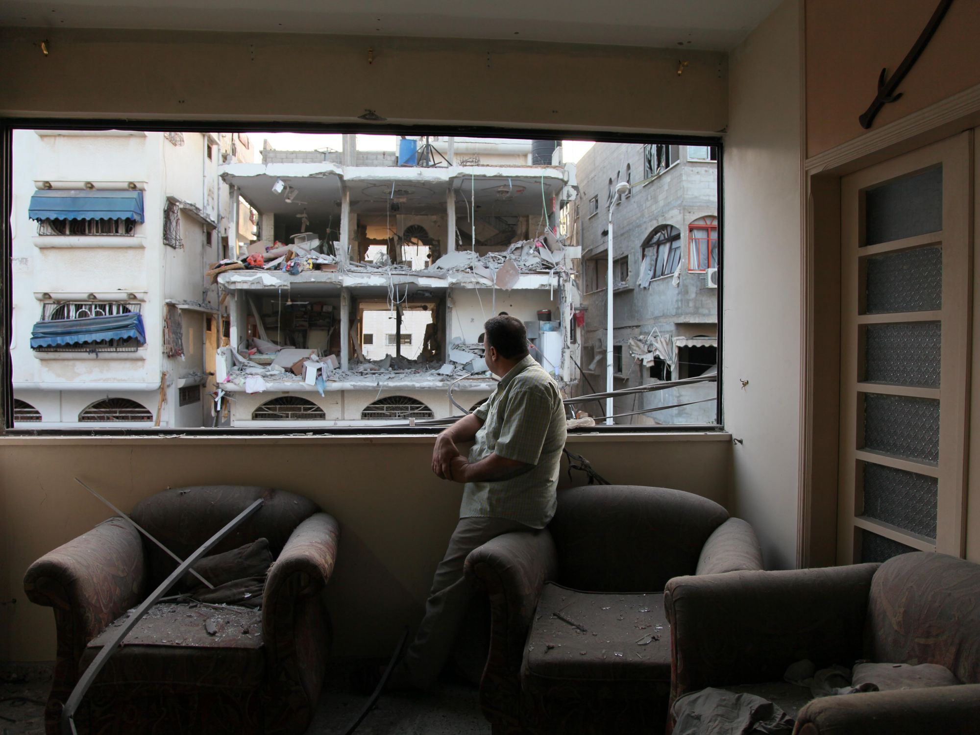 Photo of a Palestinian man in Gaza looking out the window of a destroyed building.