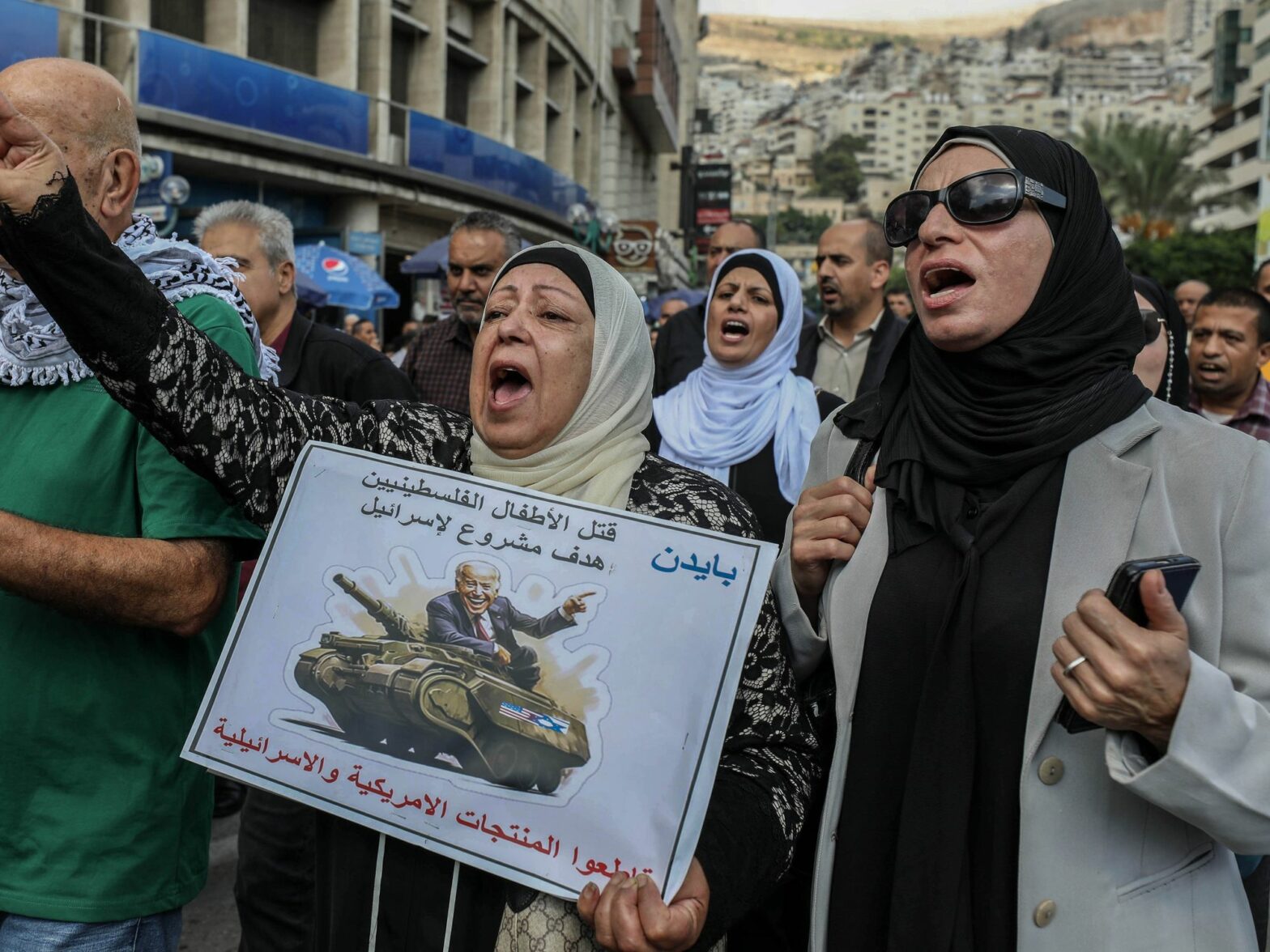 Photo of a Palestinian protestor with a sign showing the U.S. President Joe Biden riding on a military tank with an Arabic text that reads ''Killing Palestinian children is a legitimate target for Israel''