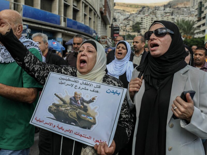 Photo of a Palestinian protestor with a sign showing the U.S. President Joe Biden riding on a military tank with an Arabic text that reads ''Killing Palestinian children is a legitimate target for Israel''