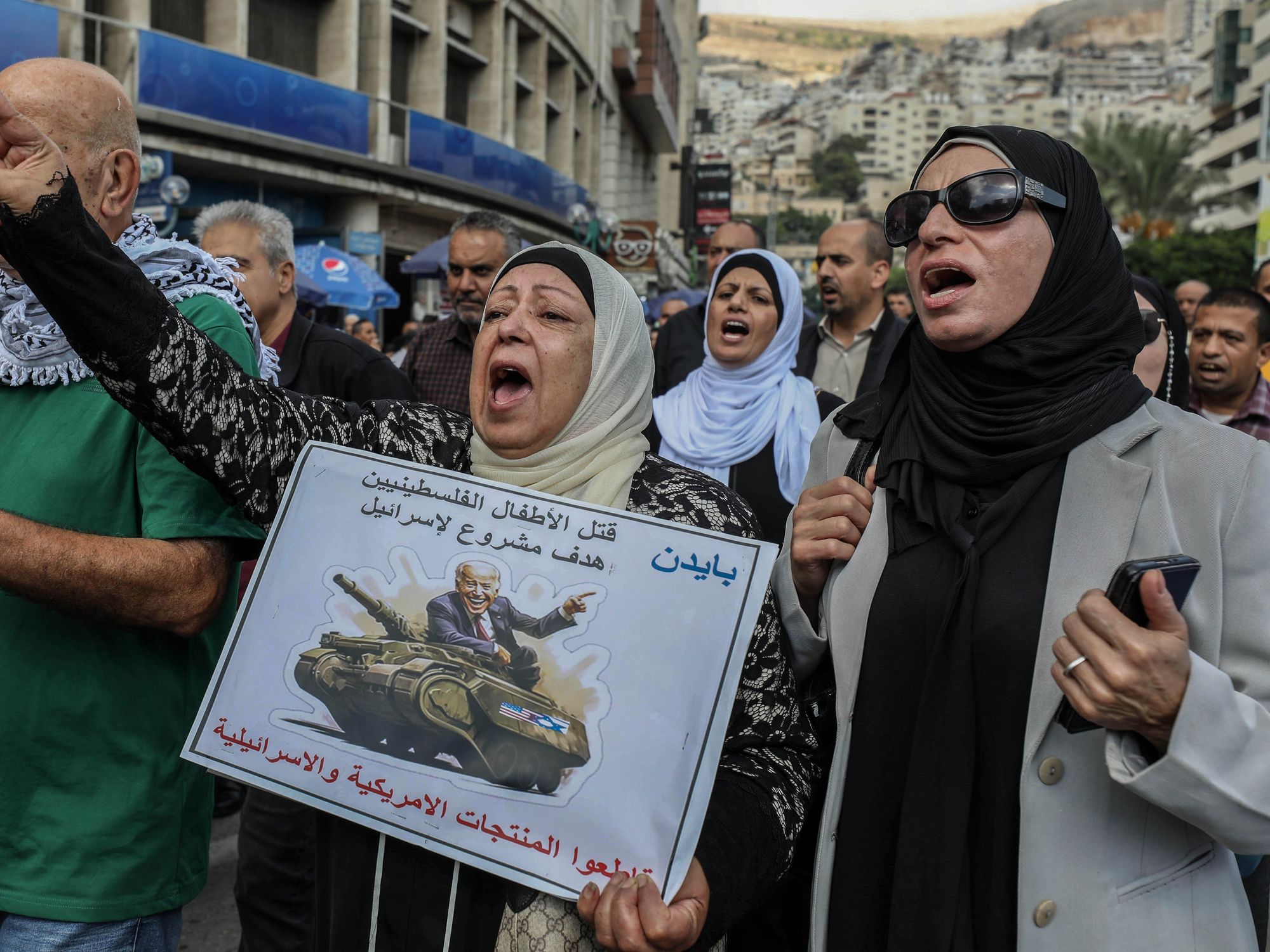 Photo of a Palestinian protestor with a sign showing the U.S. President Joe Biden riding on a military tank with an Arabic text that reads ''Killing Palestinian children is a legitimate target for Israel''