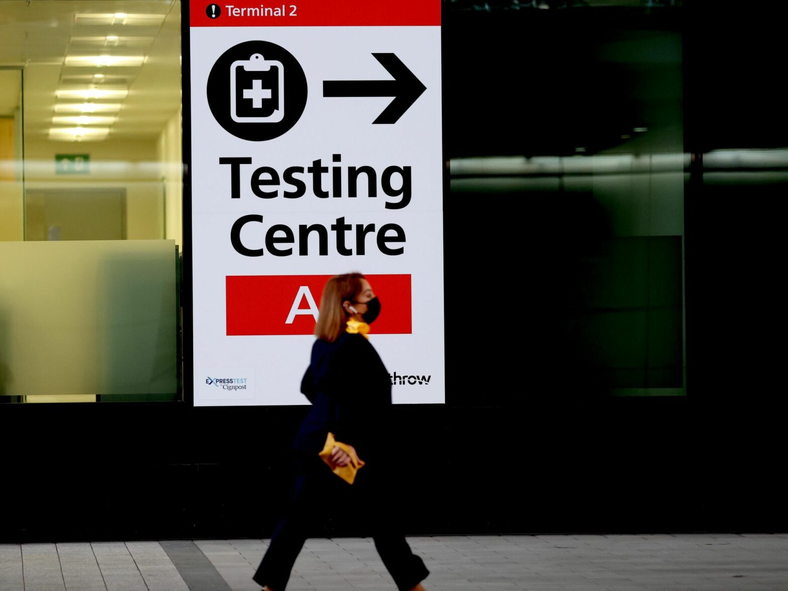 Photo of a passenger walking past a sign indicating the testing center in Heathrow Airport in London.