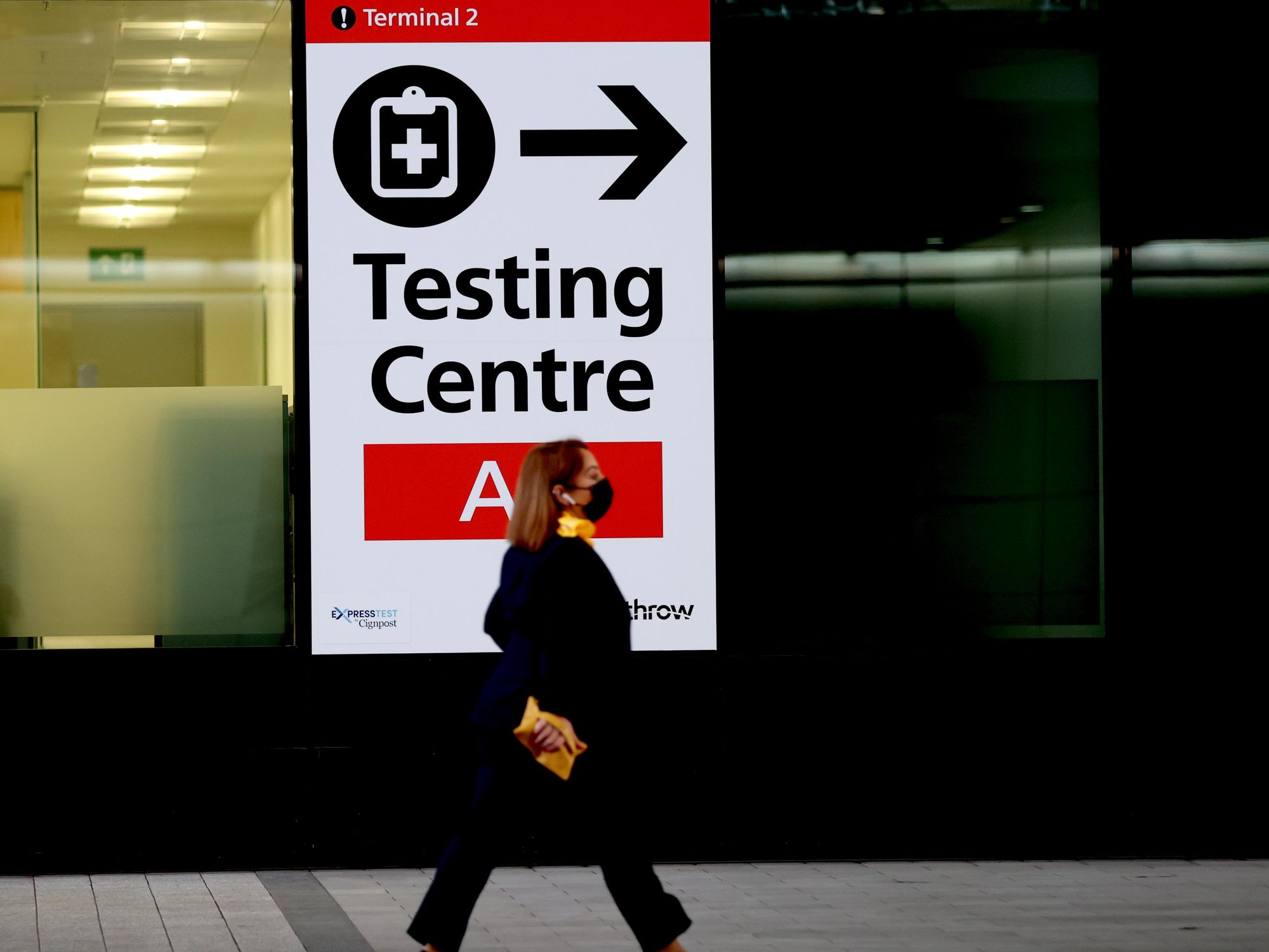Photo of a passenger walking past a sign indicating the testing center in Heathrow Airport in London.