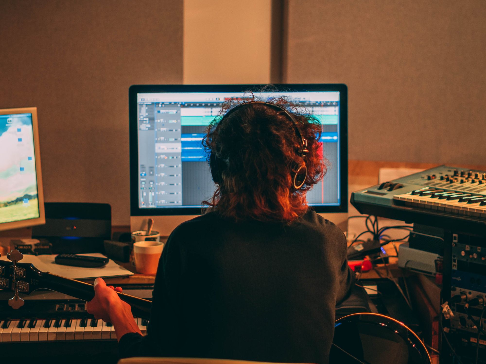 photo of a person holding a guitar and looking at a desktop computer