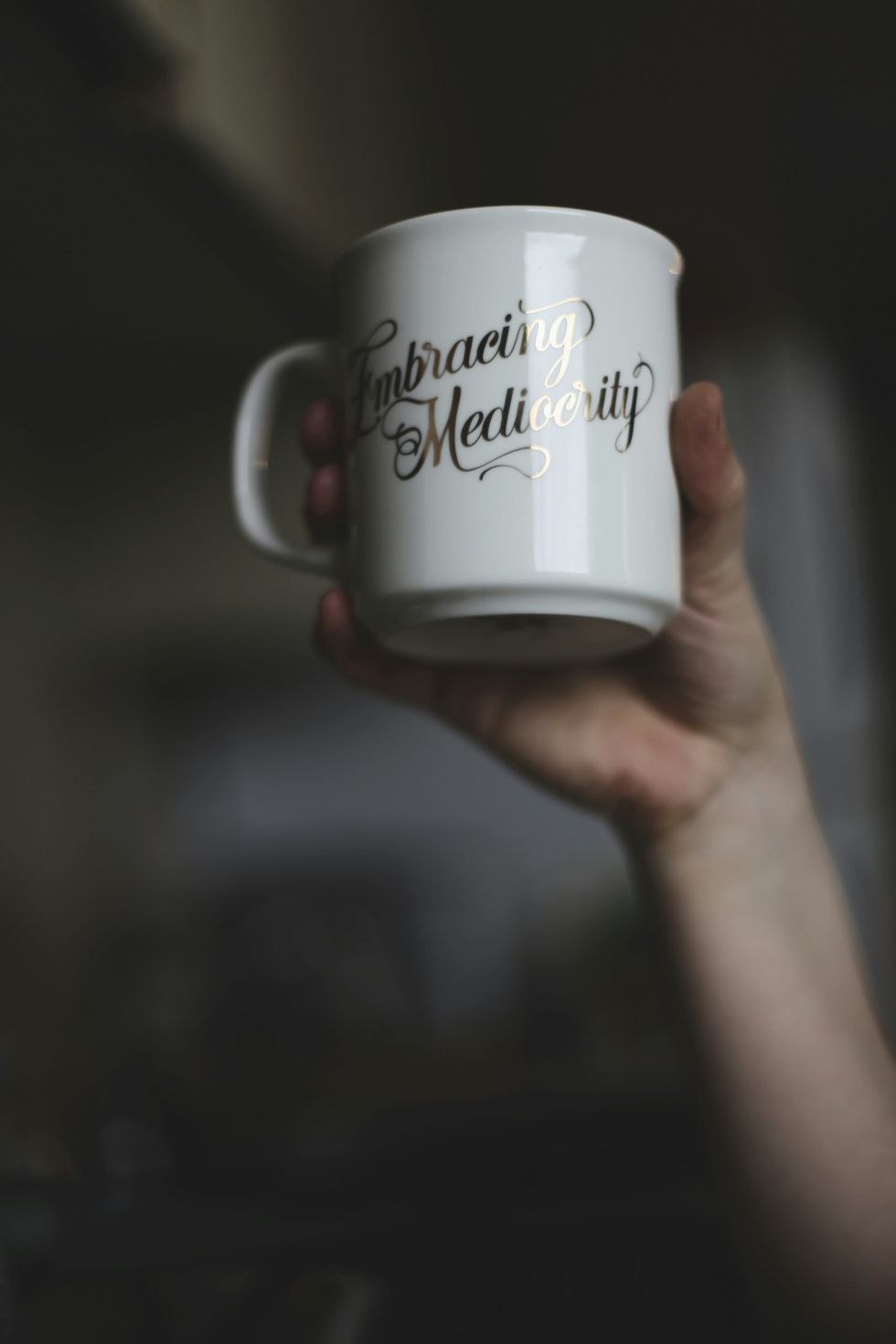 Photo of a person holding a mug that reads "embracing mediocrity"
