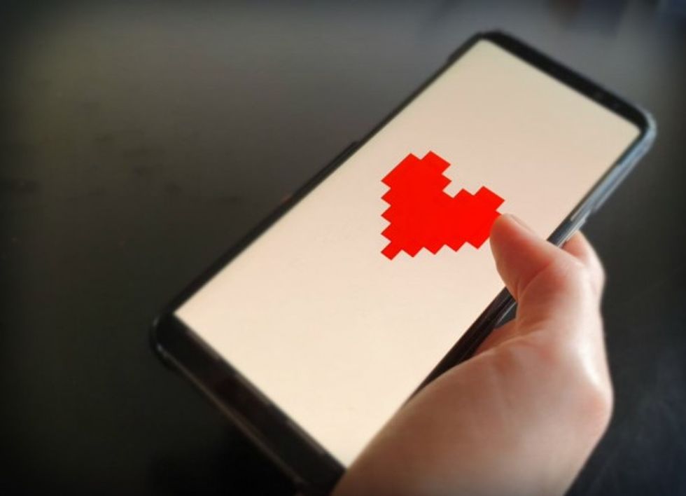 Photo of a person holding a smartphone with a big pixelated heart displayed on the screen.