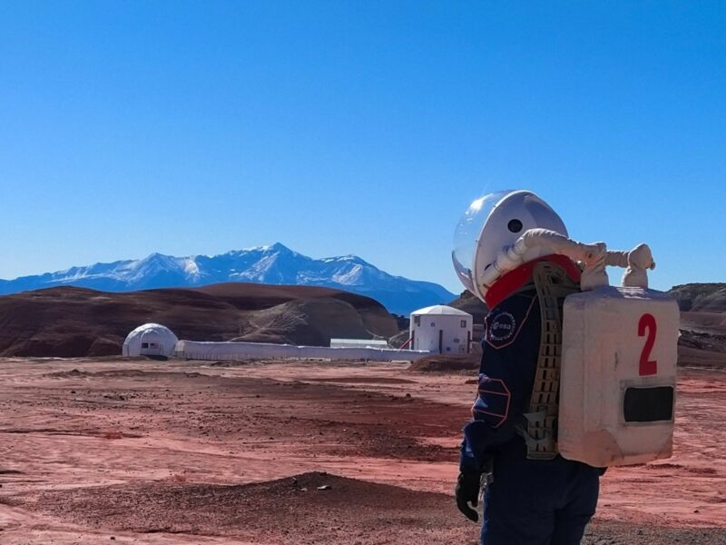 Photo of a person in a space suit walking toward the ​Mars Desert Research Station near Hanksville, Utah