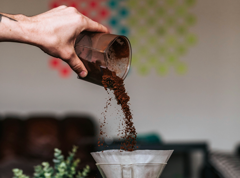 Photo of a person pouring ground coffee into a coffee maker