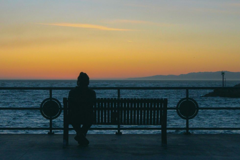 Photo of a person sitting on a bench watching the sunset