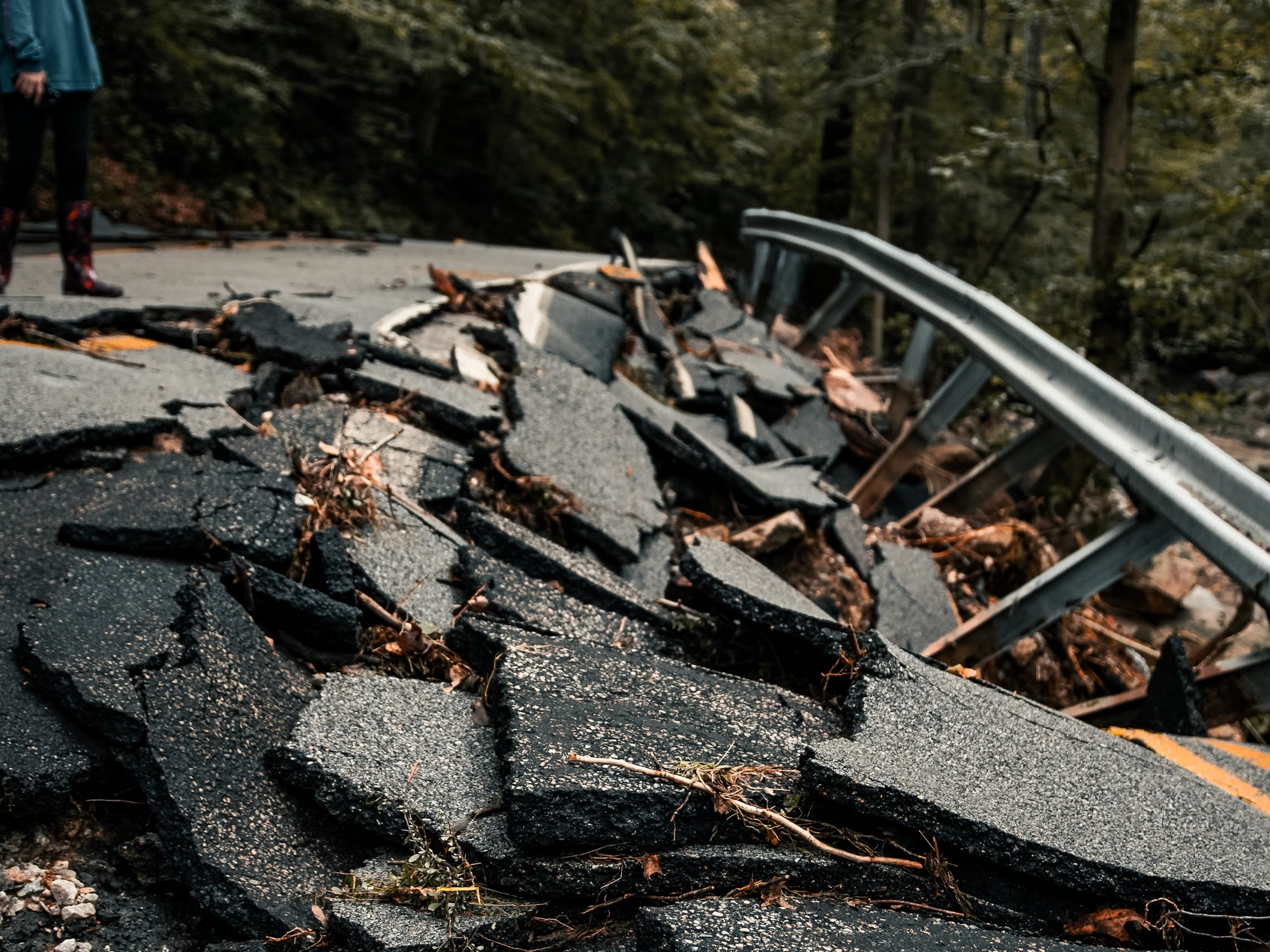 Photo of a person standing next to rubble of a road destroyed by an earthquake