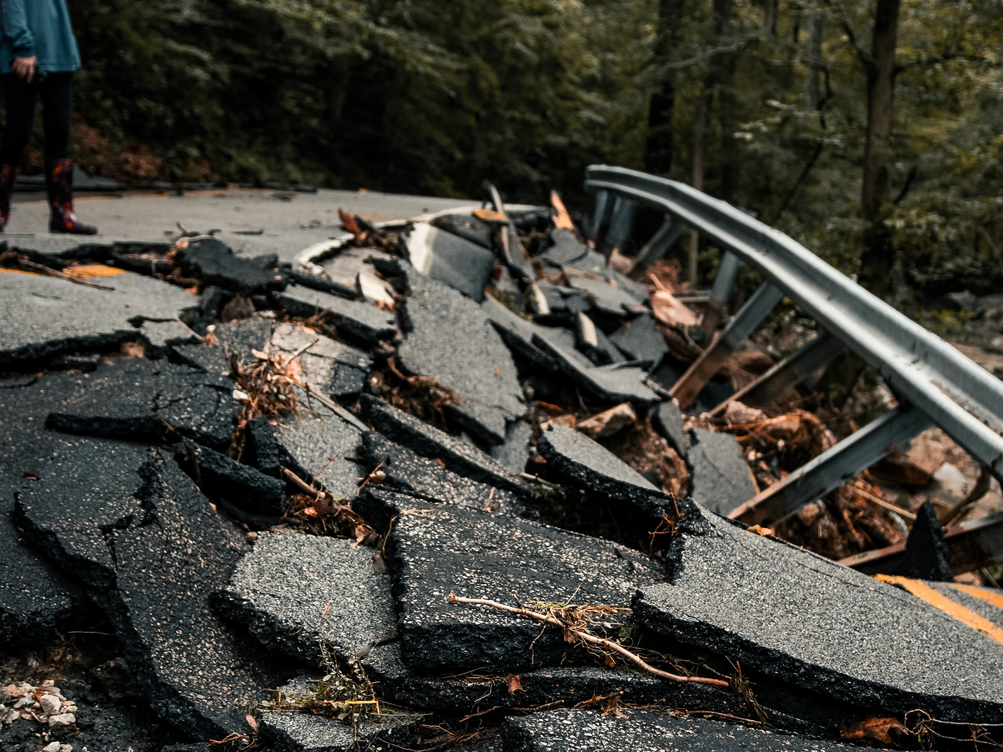 Photo of a person standing next to rubble of a road destroyed by an earthquake