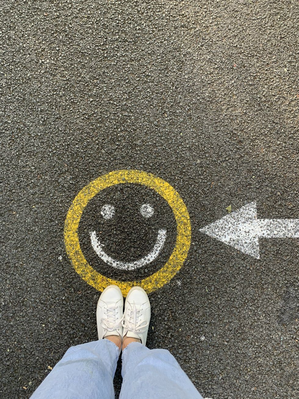 Photo of a person standing on the drawing of a smiley face on a road.