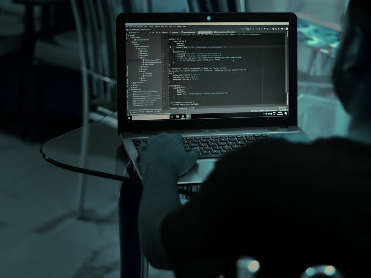 Photo of a person typing on a laptop with lines of code on the screen
