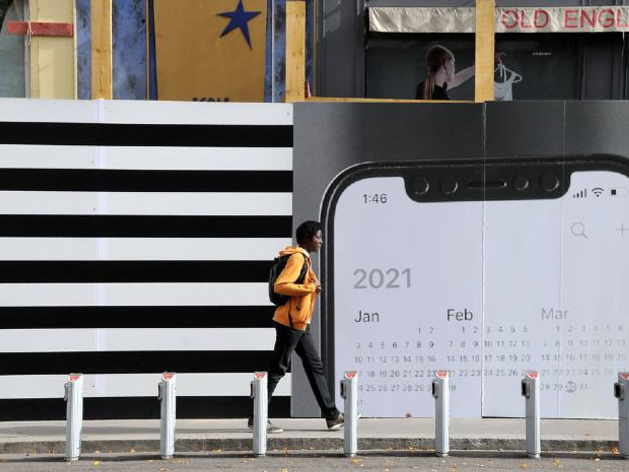 Photo of a person walking by a placard displaying a smartphone that shows a 2021 calendar