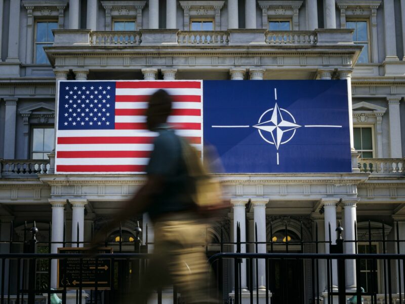 Photo of a person walking past ​U.S. and NATO flags in Washington on the sidelines of the NATO summit.