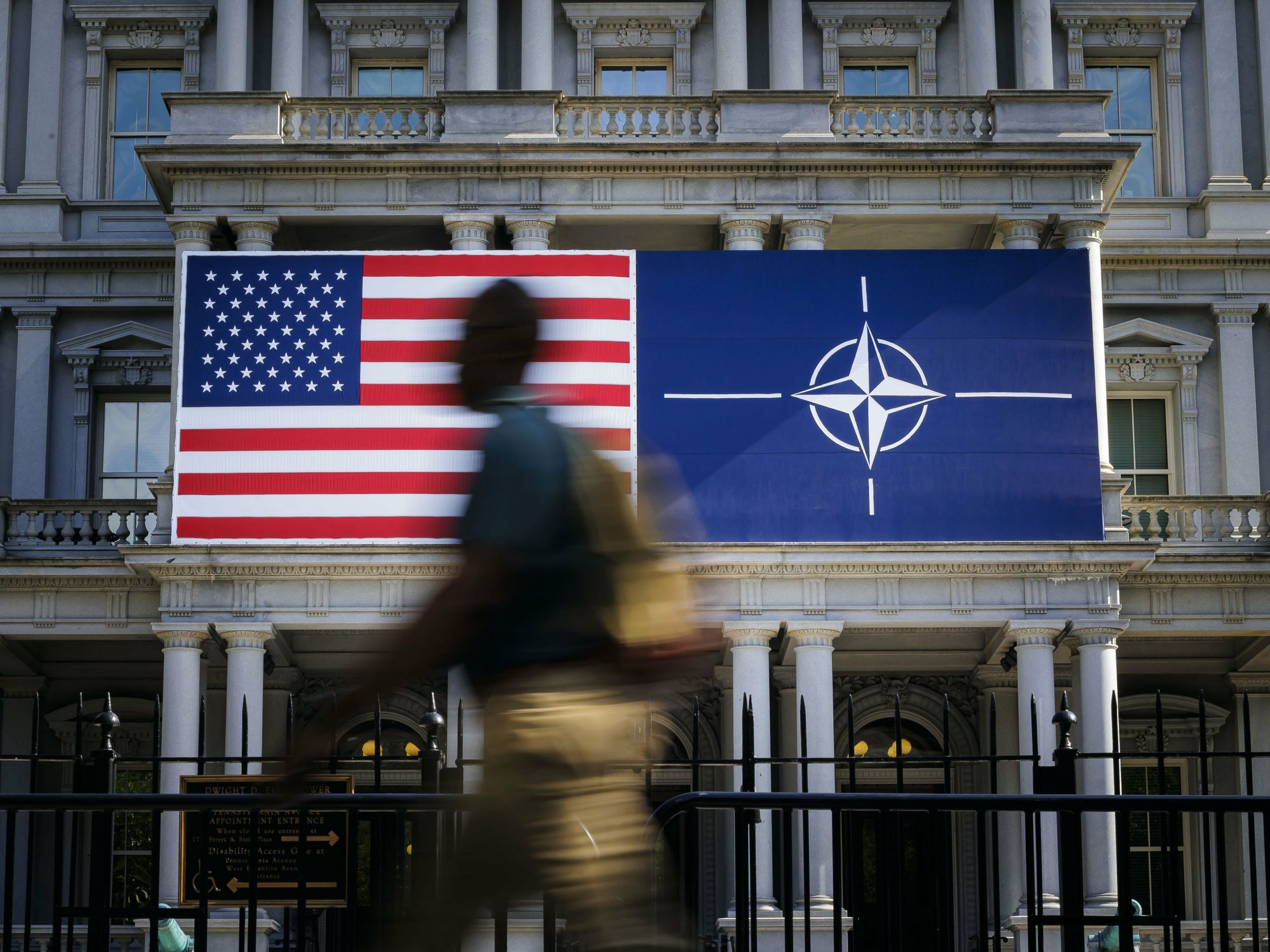 Photo of a person walking past ​U.S. and NATO flags in Washington on the sidelines of the NATO summit.
