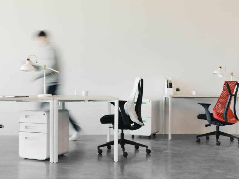 Photo of a person walking through a modern office with chairs and desks