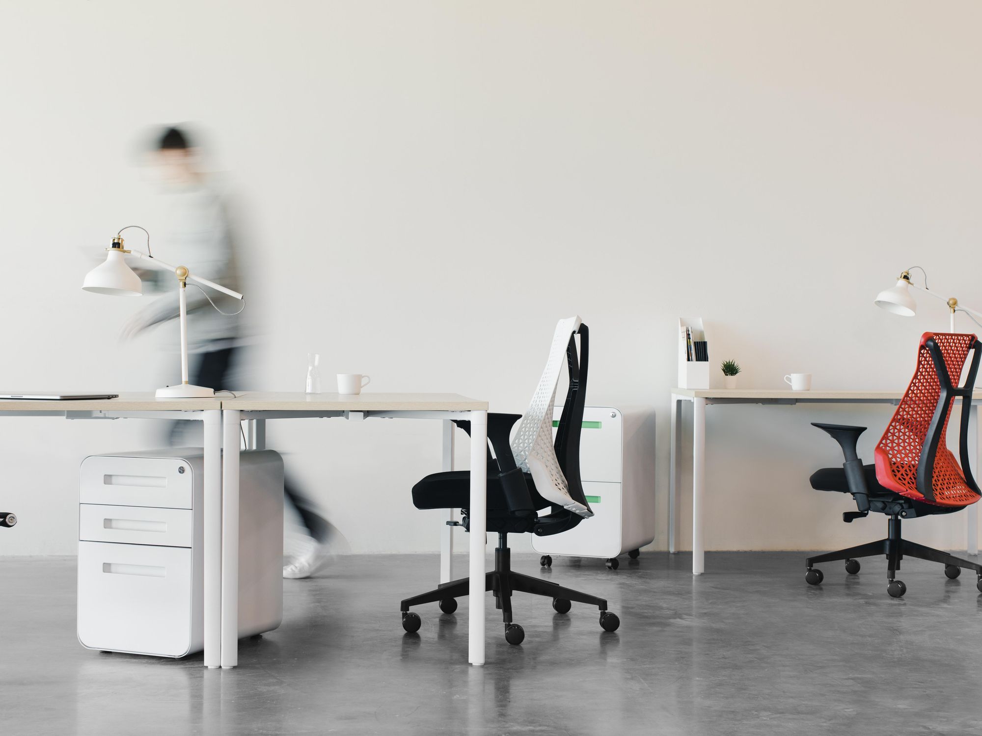 Photo of a person walking through a modern office with chairs and desks