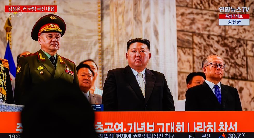 Photo of a person watching a TV screen displaying North Korean leader Kim Jong-un with officials.